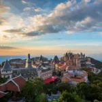 Vue panoramique d'un village de château de style européen sur une colline au coucher du soleil, entouré d'une verdure luxuriante et de montagnes lointaines, parfait pour les amateurs de voyages et d'architecture.