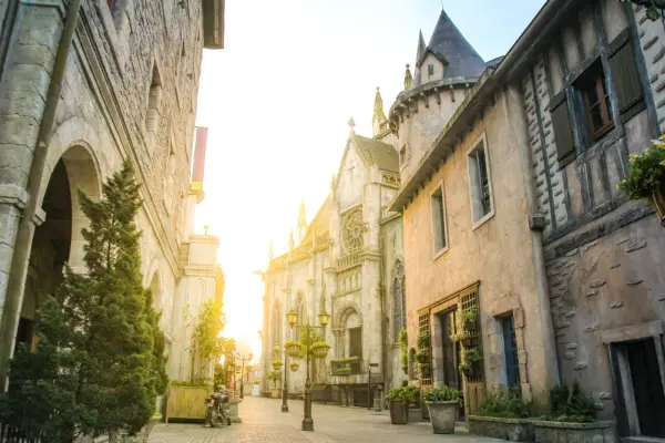 Charmante rue de style européen dans un village de château au coucher du soleil, avec des bâtiments en pierre, des tourelles et de la verdure, parfaite pour une promenade romantique ou une exploration culturelle.