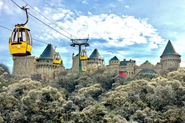 Des téléphériques baptisés « Ba Na Hills » survolent un château de conte de fées doté de multiples tourelles, situé au milieu d'une végétation dense sous un ciel partiellement nuageux, idéal pour l'aventure et le tourisme.