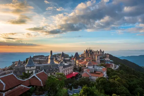 Vue panoramique d'un village de château de style européen sur une colline au coucher du soleil, entouré d'une verdure luxuriante et de montagnes lointaines, parfait pour les amateurs de voyages et d'architecture.