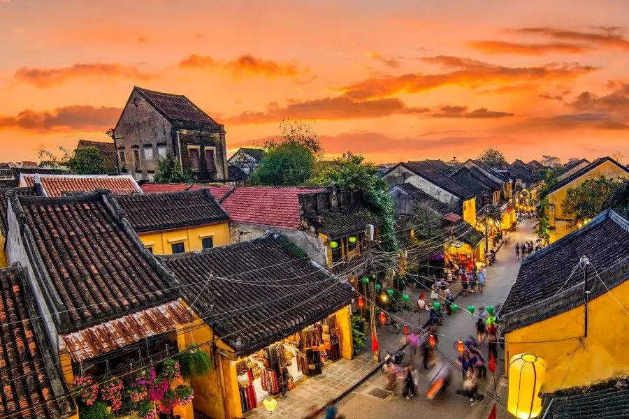 Vue du coucher de soleil sur la vieille ville de Hoi An, avec ses bâtiments jaunes, ses toits de tuiles et ses rues éclairées par des lanternes. C'est une destination incontournable pour un voyage au Vietnam en 2026.